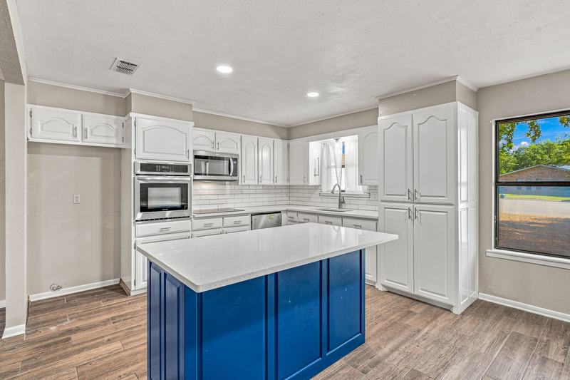 Kitchen with white cabinets, stainless appliances, and a blue center island